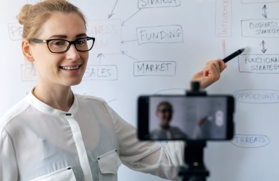 female instructor giving a live lecture via a phone video meeting and pointing to a white board