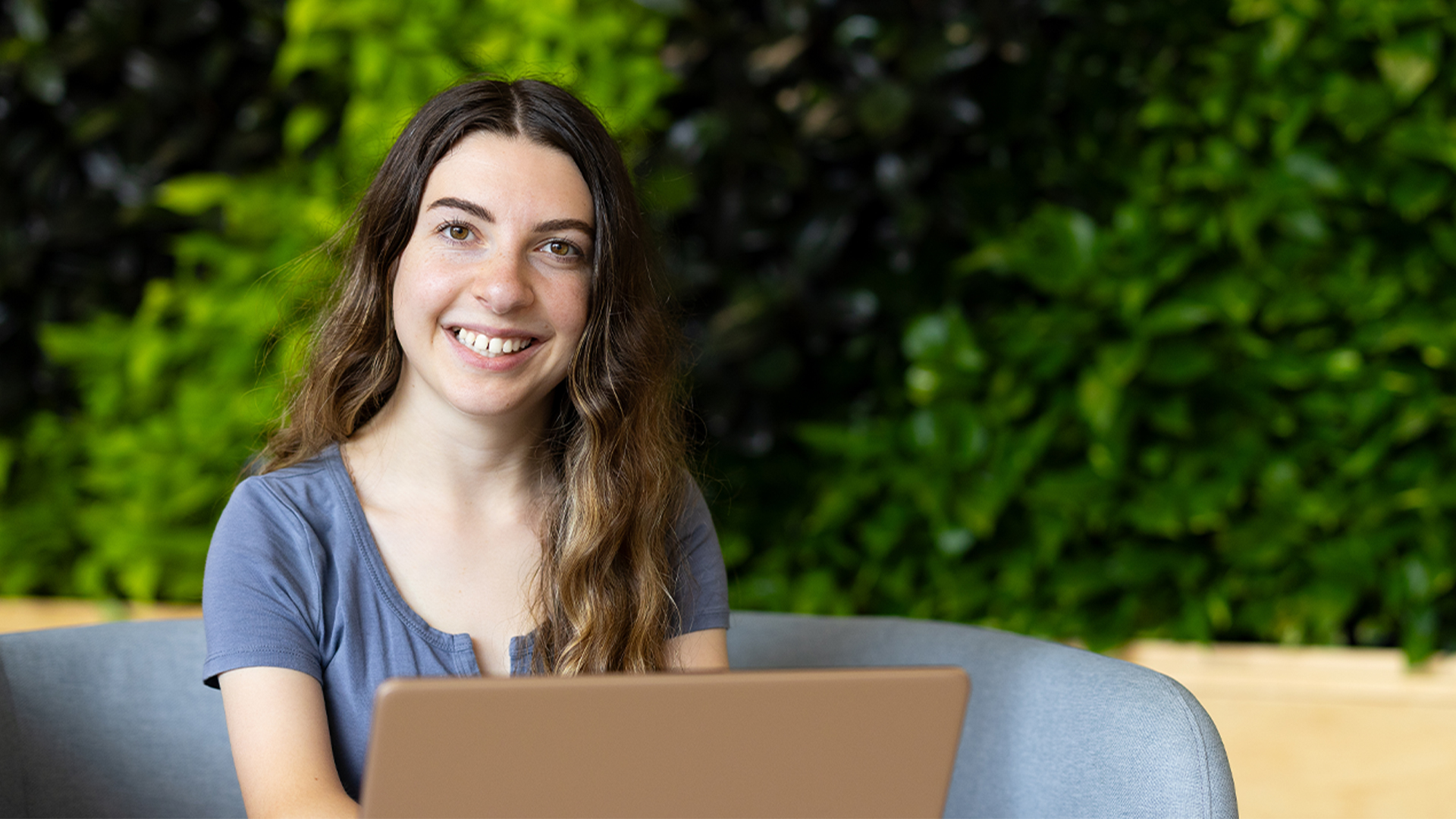 A student working at a laptop in front of a plant wall